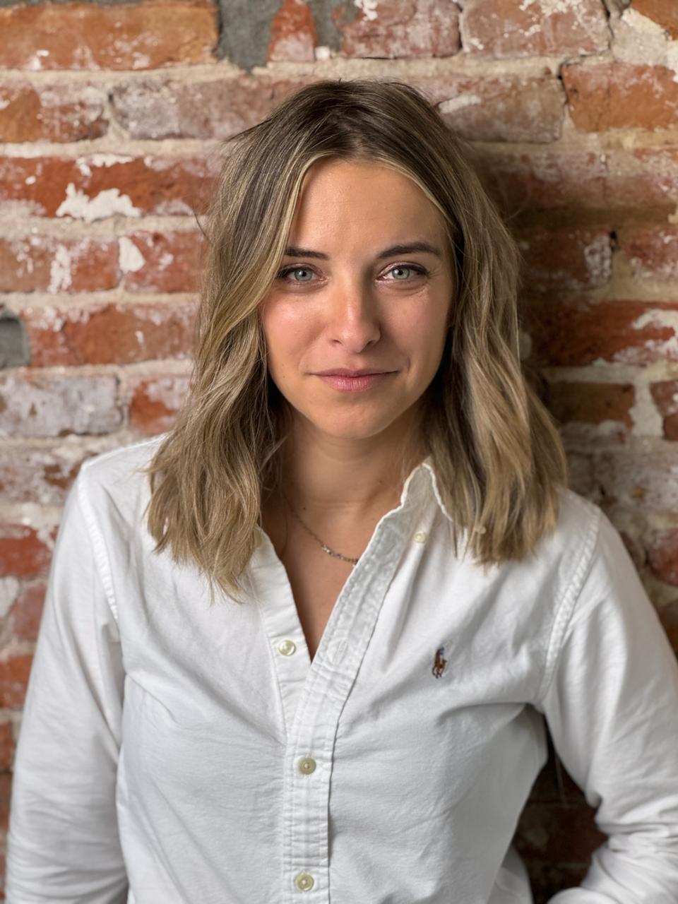 Maaike Heidweiller, founder e coach, con una camicia bianca davanti a un muro di mattoni
